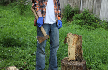 Work in the village. A guy in a checkered orange shirt and blue work gloves chops wood