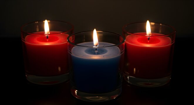 Three burning candles in glass holders glow in warm, dark lighting. For spiritual themes, holiday backgrounds, or meditative posters.
