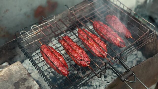 Juicy lula kebabs grilling on open fire wood barbecue. Picnic-style cooking with smoke, flames, and rustic outdoor setup