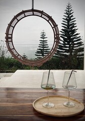 Wine glasses on a wooden table and Decorative wicker frame with mountain view.