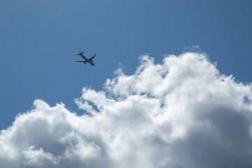 Airplane silhouette flying through blue sky with white fluffy clouds