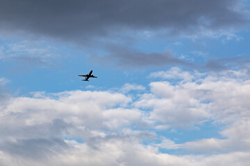 Airplane silhouette flying through blue sky with white fluffy clouds