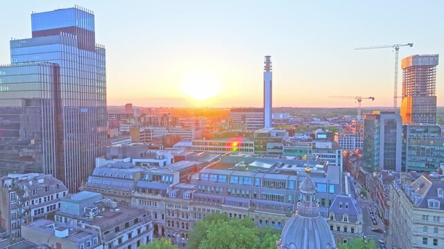 Drone footage reveals the Birmingham skyline at sunset, featuring the BT Tower, modern glass buildings, historic architecture, and cranes over a glowing cityscape.