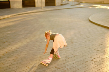 Obraz premium Young girl in pink glasses roller skating outdoors during sunset, wearing casual black top and beige skirt tied around waist, capturing playful childhood fun and lively urban atmosphere