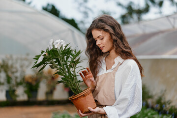 Naklejka premium Young woman in natural setting, lovingly caring for potted plant, embodying eco friendly lifestyle, happiness, and connection with nature during springtime