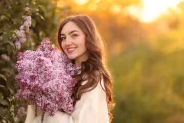 Fototapeta premium Smiling woman with bouquet of lilac flowers outdoors in morning. Space for text