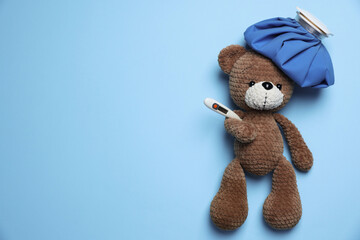 Pediatrics concept. Toy bear with ice bag and thermometer on light blue background, top view. Space for text