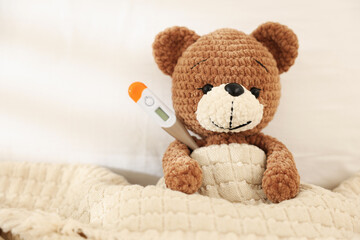 Pediatrics concept. Toy bear with thermometer in bed, space for text