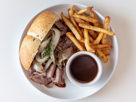 Delicious roast beef sandwich with french fries and au jus on white plate