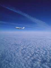 Airplane flying above clouds leaving contrail in blue sky