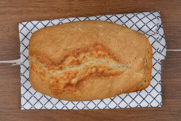 A freshly baked, rustic loaf of bread rests on a checkered kitchen towel, set against a warm wooden...