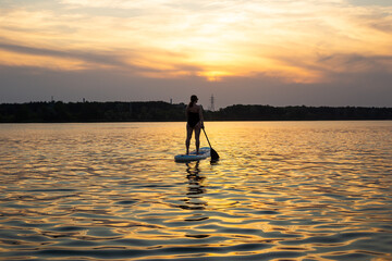 A young woman poses standing on a sup board with paddle. Sunset in the background. Copy space....