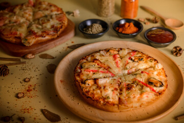 Pizza on a wooden plate placed on a table with a yellow background.