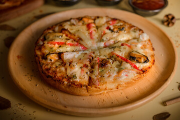 Pizza on a wooden plate placed on a table with a yellow background.