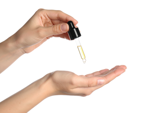 Hand holding dropper with golden liquid dropping onto open palm close up view isolated on transparent background. PNG die-cut for advertising