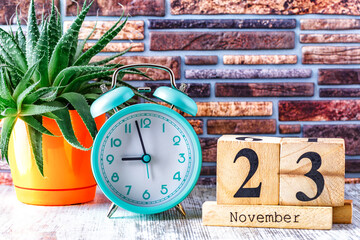 Wooden calendar with the date November 23.Monthly calendar for planning and management concept with alarm clock on wooden background