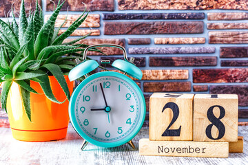 Wooden calendar with the date November 28.Monthly calendar for planning and management concept with alarm clock on wooden background