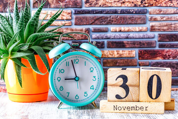 Wooden calendar with the date November 30.Monthly calendar for planning and management concept with alarm clock on wooden background