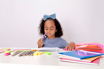 Thoughtful schoolgirl, ethnic sitting at a table with school supplies attentive to reading