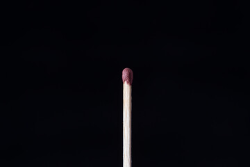  A single matchstick stands upright against a solid black background