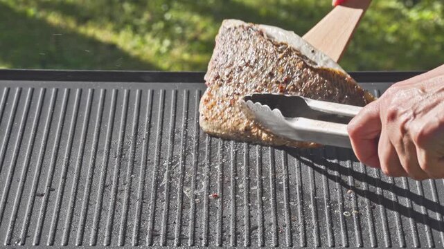 outdoor cooking. cook preparing fresh sea bream fish fillet with spices on hot grill pan for making delicious meal in garden, food closeup, outdoors natural light