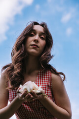 Low angle portrait of young woman holding roses against blue sky