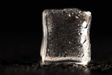 A single, clear ice cube, visibly melting and covered in condensation droplets, set against