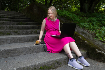 Young woman works on her laptop in a summer park, her pet agama lizard lounging peacefully beside her on a delicate leash