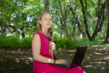 Young woman working on her laptop in a summer park gently cradles her harnessed agama lizard in a tender embrace