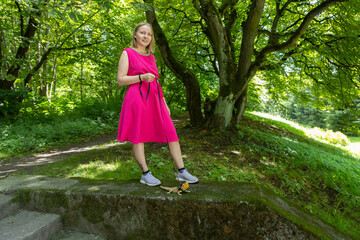 Young woman strolls through a summer park with her agama lizard on a delicate leash
