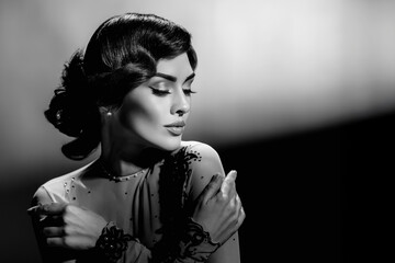 Black and white portrait of gorgeous young woman with wavy hair posing in elegant evening dress. Retro beauty shot in black and white with styled waves and dramatic Harcourt-inspired lighting