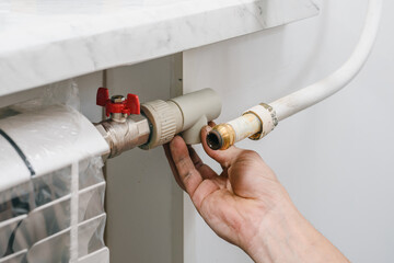 Closeup of male plumber installing connecting element bypass valve. Technician adjusting the bypass system while installing a new heating radiator in an apartment.