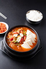 Korean food (Kimchi Jjigae), Kimchi soup with tofu, pork, scallion and chili in Korean stone bowl eating with cooked rice and fresh kimchi on black background