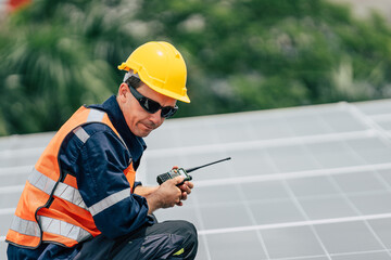 Worker in hard hat and safety gear inspects solar panels on rooftop during bright day