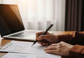 Person writing on financial report next to laptop