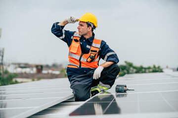 Worker installs solar panels on rooftop while wearing helmet and safety gear during overcast day in...