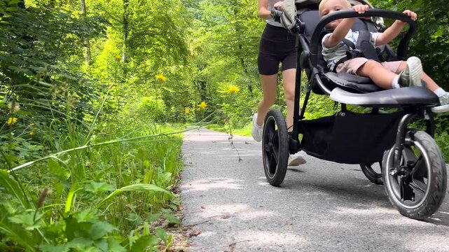 Woman running in the park with a small child in an outdoor stroller. Sports and parenting, time with a baby and jogging