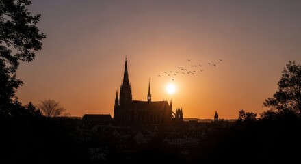 Naklejka premium Dramatic Silhouette of a Cathedral Against a Fiery Sunset Sky with Birds Flying