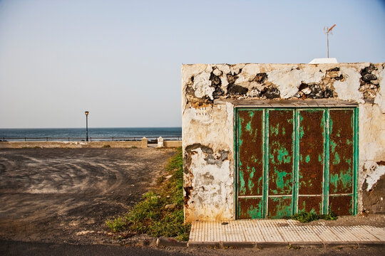 Weathered coastal structure with peeling paint and industrial setting in background, highlighting decay, shoreline infrastructure and urban periphery transformation.