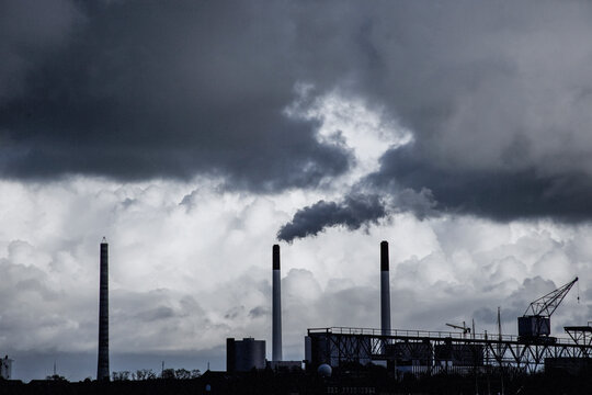 Industrial skyline in London with smoking chimneys under dramatic clouds, representing pollution, energy production and urban environmental challenges in contemporary cityscape.