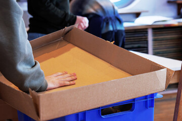 Student folding cardboard for reuse or recycling. Preparing carton packaging for disposal. A person...