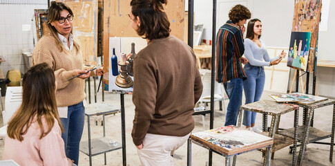Female teacher working with art students during painting class at university college - Back to school and campus lifestyle concept - Soft focus on woman face