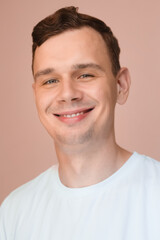 Obraz premium Smiling young man in a white t-shirt on a soft pink background. Friendly and relaxed portrait.