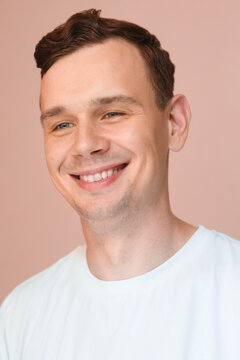 Smiling young man in a white t-shirt on a soft pink background. Friendly and relaxed portrait.