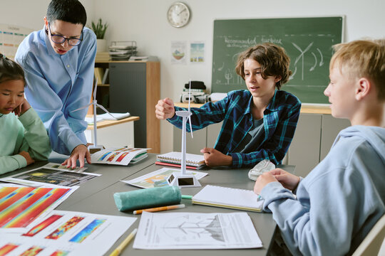 Group of multiethnic teenagers collaborating on science project with Caucasian female teacher assisting, students assembling model wind turbines and discussing renewable energy concepts in classroom