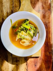 served in a white plastic bowl on a wooden cutting board isolated on a wooden table in the morning sun, vegetable tamarind with leafy and very fresh cabbage eaten as breakfast, indonesian food