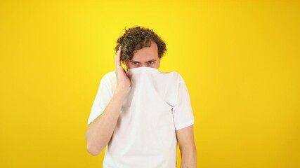 Shy man hides his face in his shirt collar on a vivid yellow background perfect for social anxiety campaigns, mental health promotions, therapy ads, confidence ads, and World Mental Health Day.