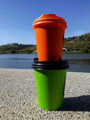 Obraz premium Two disposable portable paper coffee cups of different sizes and colors with plastic lids on background of beautiful nature. Take-Out Coffee. Close-up. Vertical photo