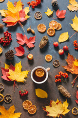 Autumn mood flat lay with cup of tea, fallen leaves, red berries, apples, cones on dark table background. Happy holidays, thanksgiving day, cozy home weekend. Hygge flat lay, top view, overhead.