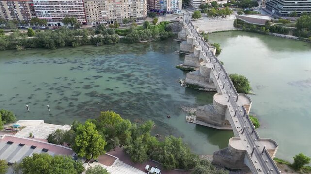 Aerial view of the Puente de Piedra bridge crossing the river, displaying a mix of stone textures and reflections in the water, Zaragoza, Aragon, Spain.